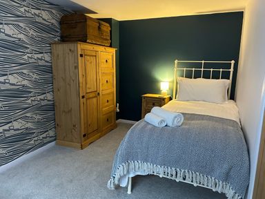 A bedroom with a single bed a wooden wardrobe and a bedside table with a lamp at Secret Garden 34C Clarence Street Dartmouth