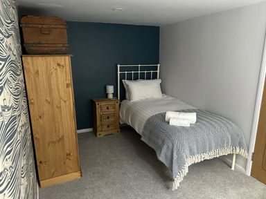 A bedroom with a single bed a wooden wardrobe and a bedside table with a lamp at Secret Garden 34C Clarence Street in Dartmouth