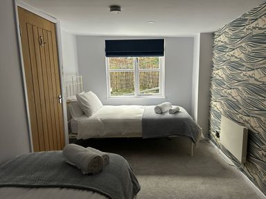A bedroom with two single beds next to a window and a wooden door at Secret Garden 34C Clarence Street in Dartmouth