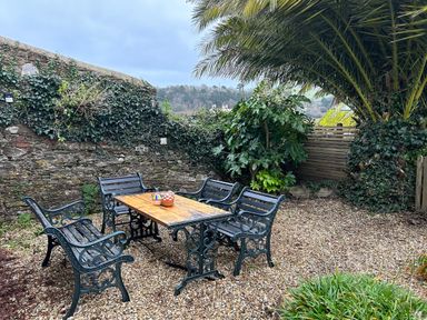 An outdoor seating area with a wooden table and metal benches surrounded by plants and a stone wall at Secret Garden 34C Clarence Street in Dartmouth