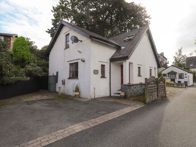 White cottage with satellite dish and small garden area beside a narrow street at Cherry Tree Cottage in Windermere
