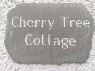 A carved stone sign with the text Cherry Tree Cottage on a textured white wall at Cherry Tree Cottage in Windermere