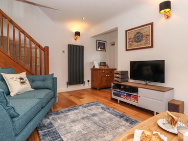 A living room with a blue sofa next to wooden stairs a TV on a cabinet and a table with pastries at Cherry Tree Cottage in Windermere