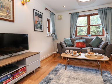 A living room with a gray sofa and coffee table with breakfast items a television on a wooden cabinet and blue curtains at Cherry Tree Cottage in Windermere