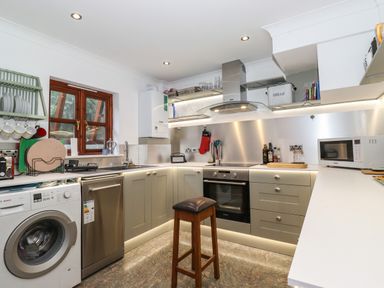 A kitchen with appliances including washing machine dishwasher microwave oven and a stool at Cherry Tree Cottage in Windermere