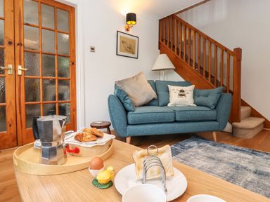 A living room with a blue sofa next to wooden stairs and a coffee table set with breakfast items at Cherry Tree Cottage in Windermere