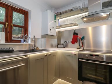 A kitchen with a sink, stove, oven, and shelves with glasses at Cherry Tree Cottage in Windermere
