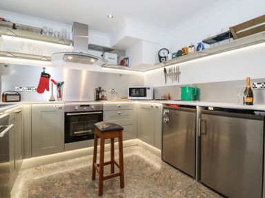 A kitchen with a wooden stool a built-in oven stainless steel fridge microwave and shelves with kitchen items at Cherry Tree Cottage in Windermere