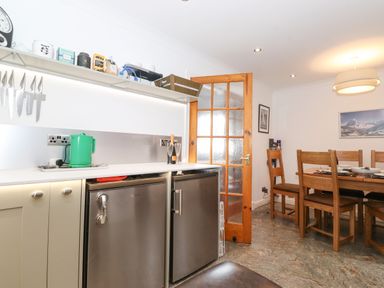 A kitchen counter with knives on a magnetic strip and dining table with wooden chairs at Cherry Tree Cottage in Windermere
