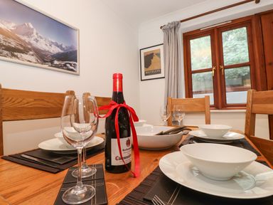 A dining table with wine bottle glasses and bowls in a room with wooden chairs window and mountain pictures at Cherry Tree Cottage in Windermere
