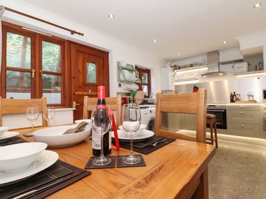 A kitchen dining area with wooden table chairs wine bottle wine glasses and stove at Cherry Tree Cottage in Windermere