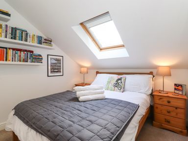 A bedroom with a bed with folded towels two bedside tables with lamps and books a skylight window and shelves with books at Cherry Tree Cottage in Windermere