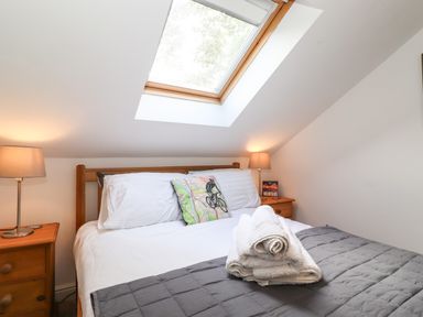 A bedroom with a double bed white sheets pillows bedside tables lamps and a skylight window at Cherry Tree Cottage in Windermere