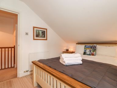 A bedroom with a wooden bed frame white bedding folded towels bedside table and framed picture on wall at Cherry Tree Cottage in Windermere