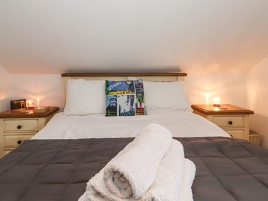 A bed with white pillows and a folded towel on a gray quilt with bedside tables and lamps at Cherry Tree Cottage in Windermere