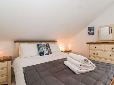 A bedroom with a bed with white and colorful pillows bedside tables with lamps and a dresser with mirror at Cherry Tree Cottage in Windermere