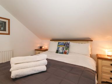 A bedroom with a bed folded towels on a blanket and bedside tables with lamps at Cherry Tree Cottage in Windermere