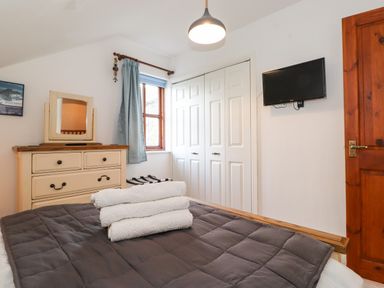 A bedroom with a bed with folded towels a dresser with a mirror a wall-mounted TV a window with curtains and a closed closet at Cherry Tree Cottage in Windermere