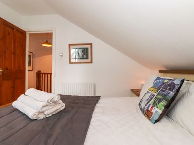 A bedroom with bed towels on a gray blanket and a colorful pillow at Cherry Tree Cottage in Windermere