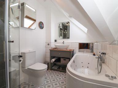 A bathroom with a toilet a shower a bathtub a sink on a wooden cabinet and a skylight at Cherry Tree Cottage in Windermere