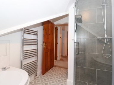 A bathroom with a towel radiator bathtub shower and wooden door at Cherry Tree Cottage in Windermere