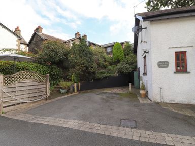 The exterior of a white building with a sign reading Cherry Tree Cottage a paved driveway and a garden with trees and bushes