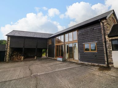 The exterior of a building with wooden cladding stone walls and large windows at Hunstone Barn in South Molton