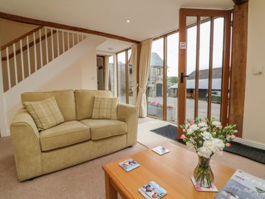 A living room with a beige sofa and coffee table with flowers near glass doors at Hunstone Barn in South Molton