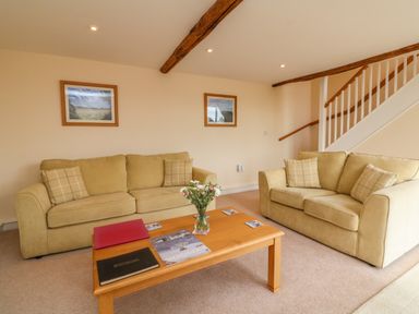 A living room with two beige sofas a wooden coffee table with books and a vase of flowers and stairs in the background at Hunstone Barn South Molton