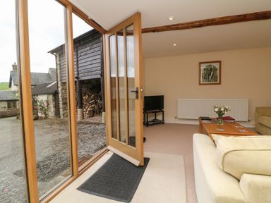 A living room with a coffee table with flowers on it and a television near an open wooden door at Hunstone Barn in South Molton