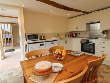 A kitchen with wooden table and chairs with cake and fruit bowl on the table at Hunstone Barn in South Molton