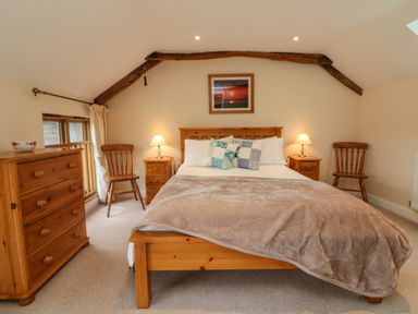 A bedroom with a wooden bed chest of drawers two chairs and bedside tables with lamps at Hunstone Barn in South Molton