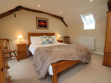 A bedroom with a wooden bed with pillows and blankets bedside tables with lamps wooden chairs a dresser and a wardrobe at Hunstone Barn in South Molton