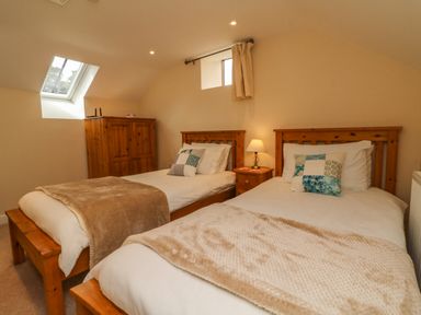 A bedroom with two single wooden beds with beige blankets and pillows a wooden wardrobe and a bedside table with a lamp at Hunstone Barn in South Molton