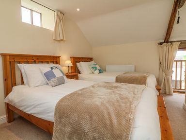A bedroom with two wooden framed beds white bedding and beige throws at Hunstone Barn in South Molton