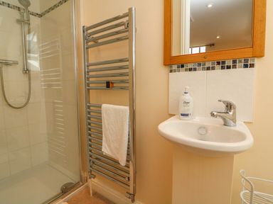 A bathroom with a shower enclosure a chrome towel rail a sink with soap and a wooden framed mirror at Hunstone Barn South Molton