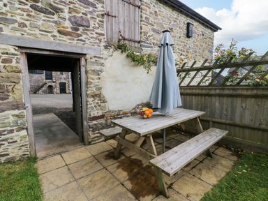 An outdoor patio area with a wooden picnic table umbrella and fruit bowl next to a stone building at Hunstone Barn in South Molton