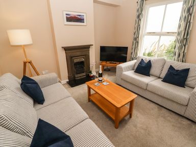 A living room with two striped sofas and a wooden coffee table with a bottle and glasses at Bay Tree Cottage in Keswick