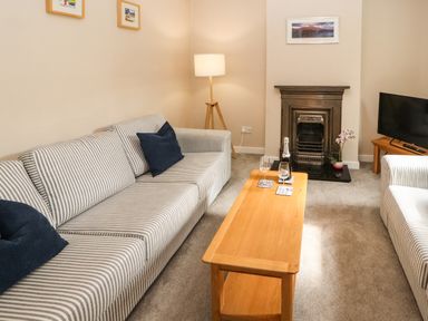 A living room with striped sofas a wooden coffee table with drinks a fireplace and a television at Bay Tree Cottage Keswick