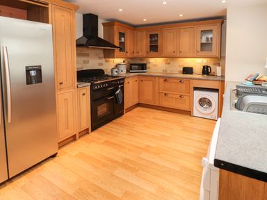 A kitchen with wooden cabinets a stainless steel refrigerator a black oven a microwave toaster kettle and a washing machine at Bay Tree Cottage in Keswick
