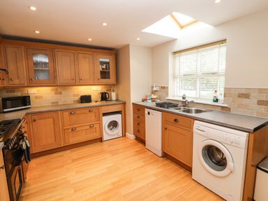 A kitchen with wooden cabinets washing machines a dishwasher a microwave and a window at Bay Tree Cottage in Keswick