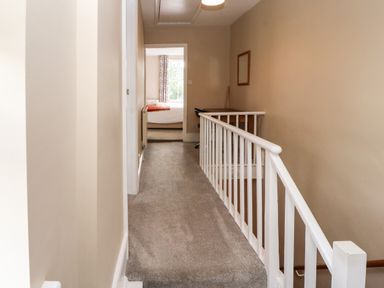 A carpeted hallway with a white railing and a desk with a chair near a bedroom at Bay Tree Cottage in Keswick