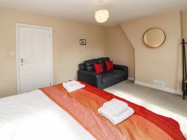 A bedroom with a bed with towels and an orange-red blanket a black sofa with red pillows and a round mirror on the wall at Bay Tree Cottage Keswick