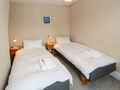 A bedroom with two single beds with white linens bedside tables with lamps and a framed picture on the wall at Bay Tree Cottage in Keswick