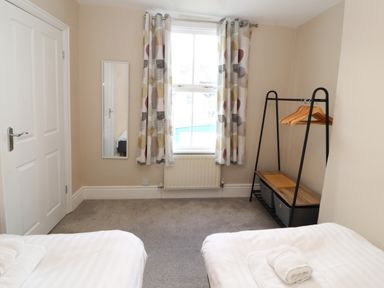A bedroom with two single beds a window with curtains a wall mirror and a clothes rack at Bay Tree Cottage in Keswick
