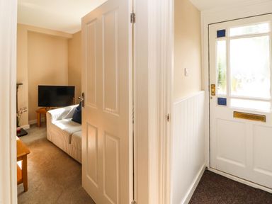 A hallway with a white door leading to a living room with a sofa a television and a wooden table at Bay Tree Cottage in Keswick