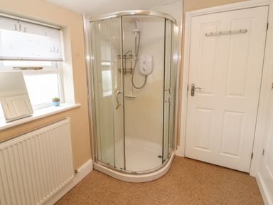 A bathroom with a corner shower enclosure a window with a roller blind a radiator and a door at Bay Tree Cottage Keswick