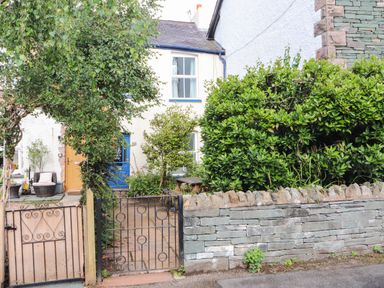 A front garden with a stone wall a metal gate wooden gate plants and two doors on a house at Bay Tree Cottage Keswick