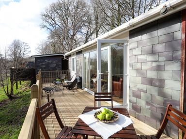 A wooden deck with outdoor chairs and a table with green apples at Treetops in Caernarfon
