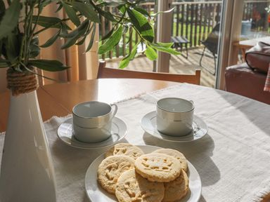 A dining table with a white vase with leaves two empty cups and saucers and a plate of biscuits at Treetops in Caernarfon